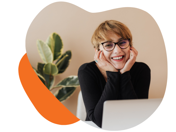 Frau lächelt freundlich in die Kamera. Sie sitzt am Tisch vor einem Laptop.